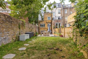 Ein Wohngrundstück mit Backsteinmauer, Holzzaun und einer Terrasse mit Gartenmöbeln.
