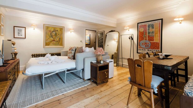 A hotel room with a bed, a desk, a chair, a dining table, and a poster on the wall. - Farmhouse Chic Studio Flat with Private Garden (Greater London)