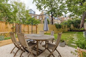 Ein runder Holztisch mit Stühlen, ein Holzzaun und ein Garten mit trittfesten Steinen.