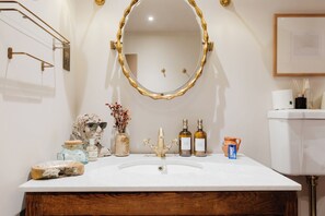 Ein Badezimmer mit einem weißen Waschbecken, einem spiegel mit goldener Rahmung und verschiedenen Pflegeprodukten.