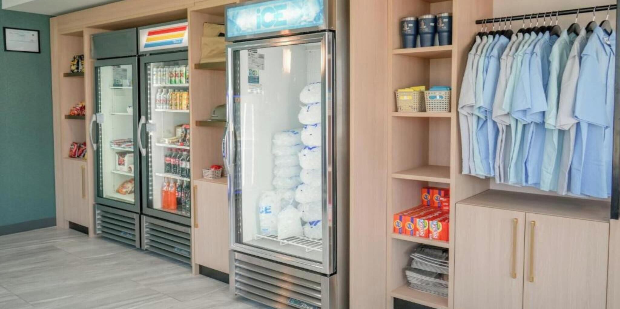 A hotel room with a minibar, a refrigerator, a clothing rack, and shelves with various items.