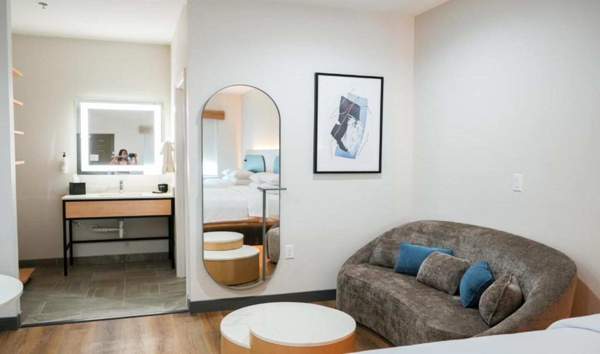 Une chambre d’hôtel moderne, dotée d’un grand miroir, d’un lit, d’un canapé et d’un tableau encadré au mur.