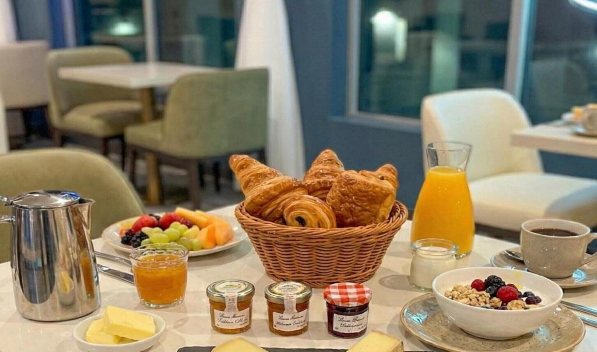 Une table dressée pour le petit-déjeuner avec des croissants, des fruits, du miel, de la confiture et du café.