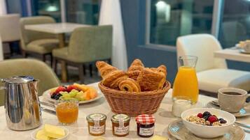 Une table dressée pour le petit-déjeuner avec des croissants, des fruits, du miel, de la confiture et du café.