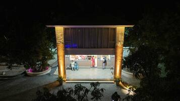 A building with a covered entrance, large columns, and a seating area with people inside.