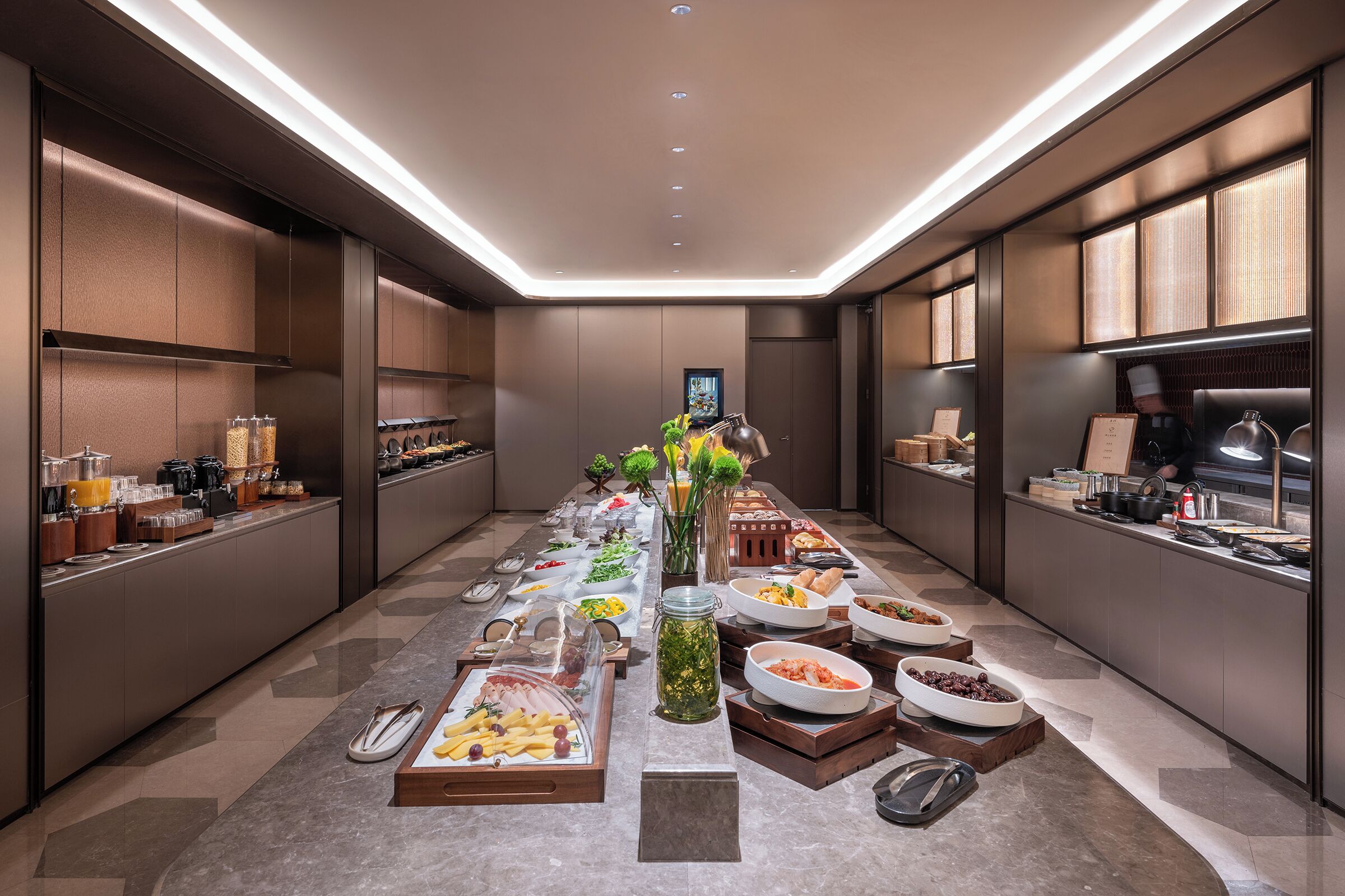Un espace buffet bien éclairé, où une grande variété d’aliments et d’ustensiles sont disposés sur une longue table.