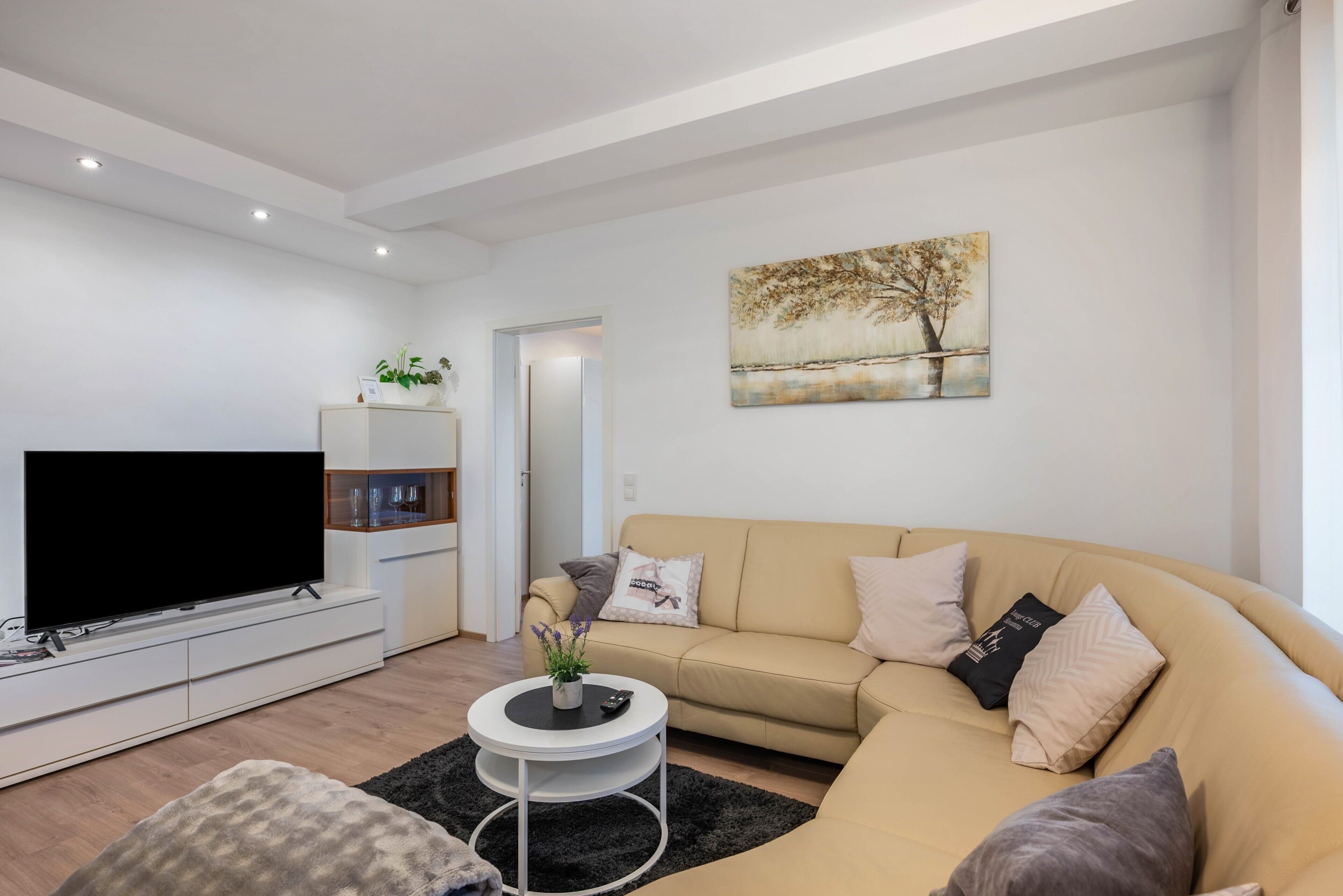 Een moderne woonkamer met een flatscreen televisie, een beige bank, een salontafel en een schilderij aan de muur.