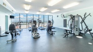 Ein Fitnessraum mit Cardiogeräten, Gewichtstrainern und großen Fenstern mit Blick auf den Strand.