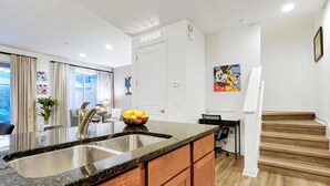 A kitchen with a granite countertop, stainless steel sink, wooden cabinets, a bowl of fruit, and a refrigerator. - Remodeled home, Regal Oaks-September Special Price (Kissimmee)