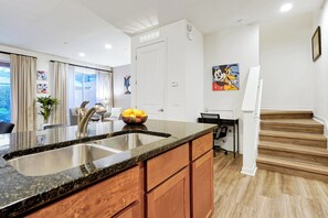 A kitchen with a granite countertop, stainless steel sink, wooden cabinets, a bowl of fruit, and a refrigerator. - Remodeled home, Regal Oaks-September Special Price (Kissimmee)