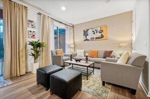 Ein modernes Wohnzimmer mit einer Couch, zwei schwarzen Hocker, einem Couchtisch und einem großen Fenster mit Vorhängen.