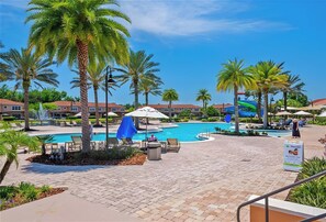 A resort pool area with palm trees, lounge chairs, and a blue umbrella. - Remodeled home, Regal Oaks-September Special Price (Kissimmee)