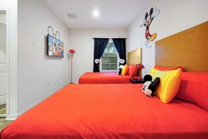 Quarto de hotel com duas camas, um adesivo de parede do Mickey Mouse, uma janela com cortinas e um bichinho de pelúcia do Mickey Mouse sobre uma das camas.