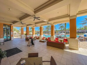 A covered outdoor seating area with a pool view, featuring multiple seating arrangements and a clear sky. - Resort-style living, heated pool and water slides! (Kissimmee)