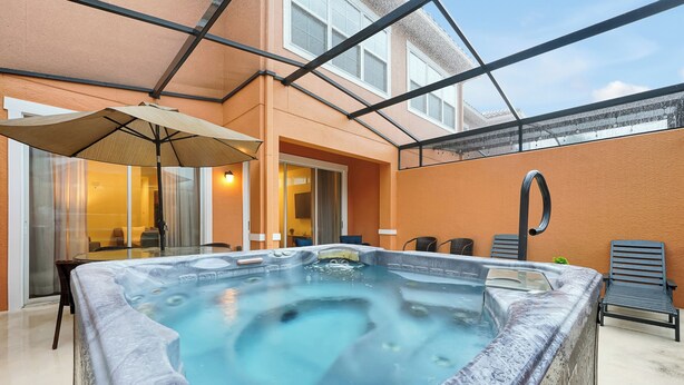 A hot tub in a covered outdoor area with a glass ceiling, a table with chairs, and a patio chair. - Remodeled home, Regal Oaks-September Special Price (Kissimmee)