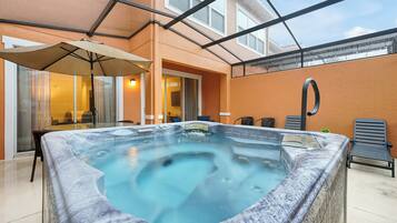 A hot tub in a covered outdoor area with a glass ceiling, a table with chairs, and a patio chair.