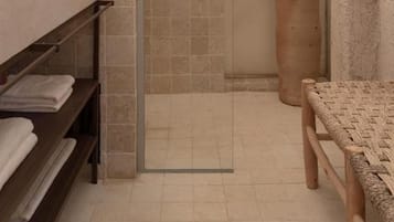 Un baño con ducha, lavamanos y estante con toallas.