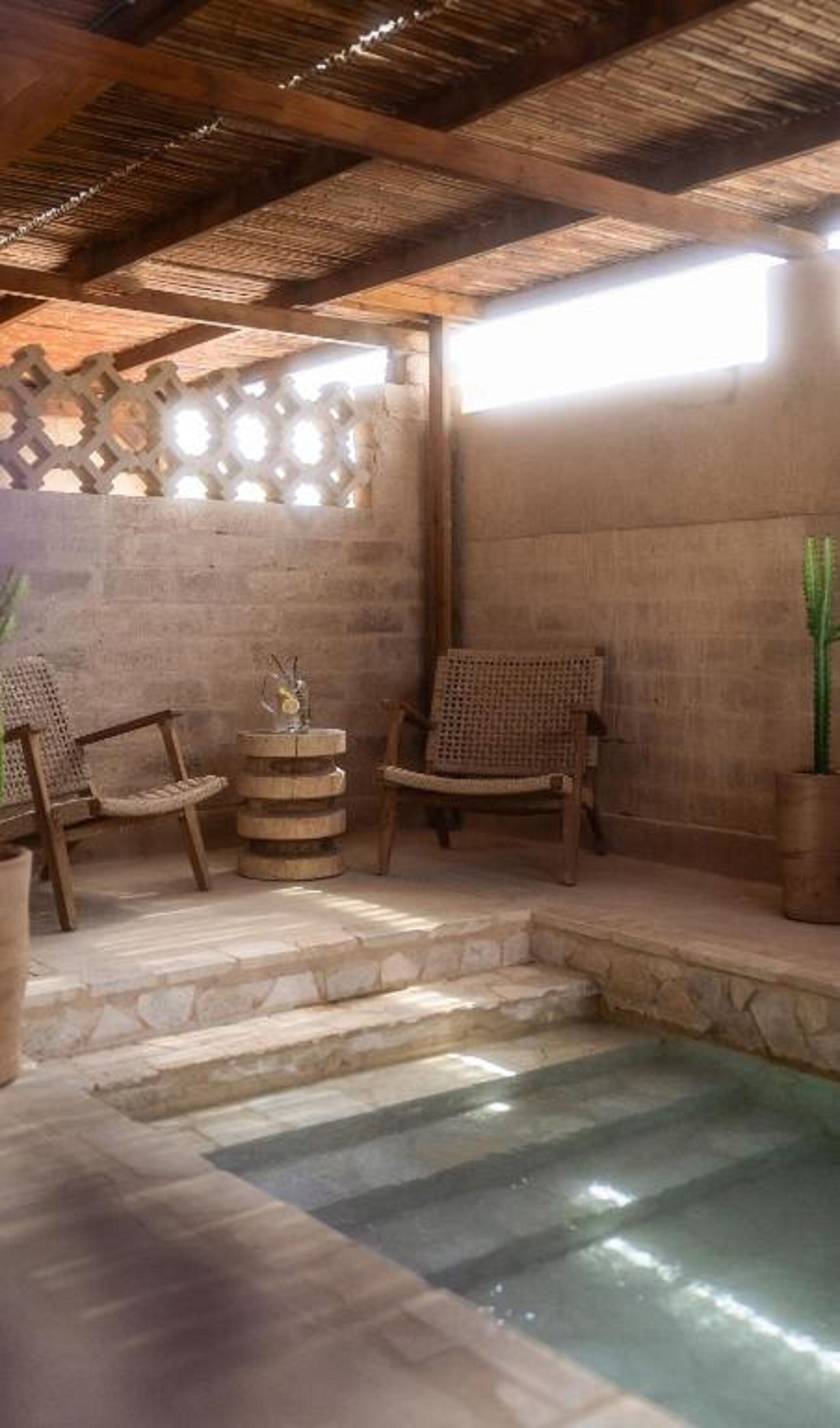 Habitación con paredes de piedra, una pequeña piscina, dos sillas de mimbre y una planta en maceta.