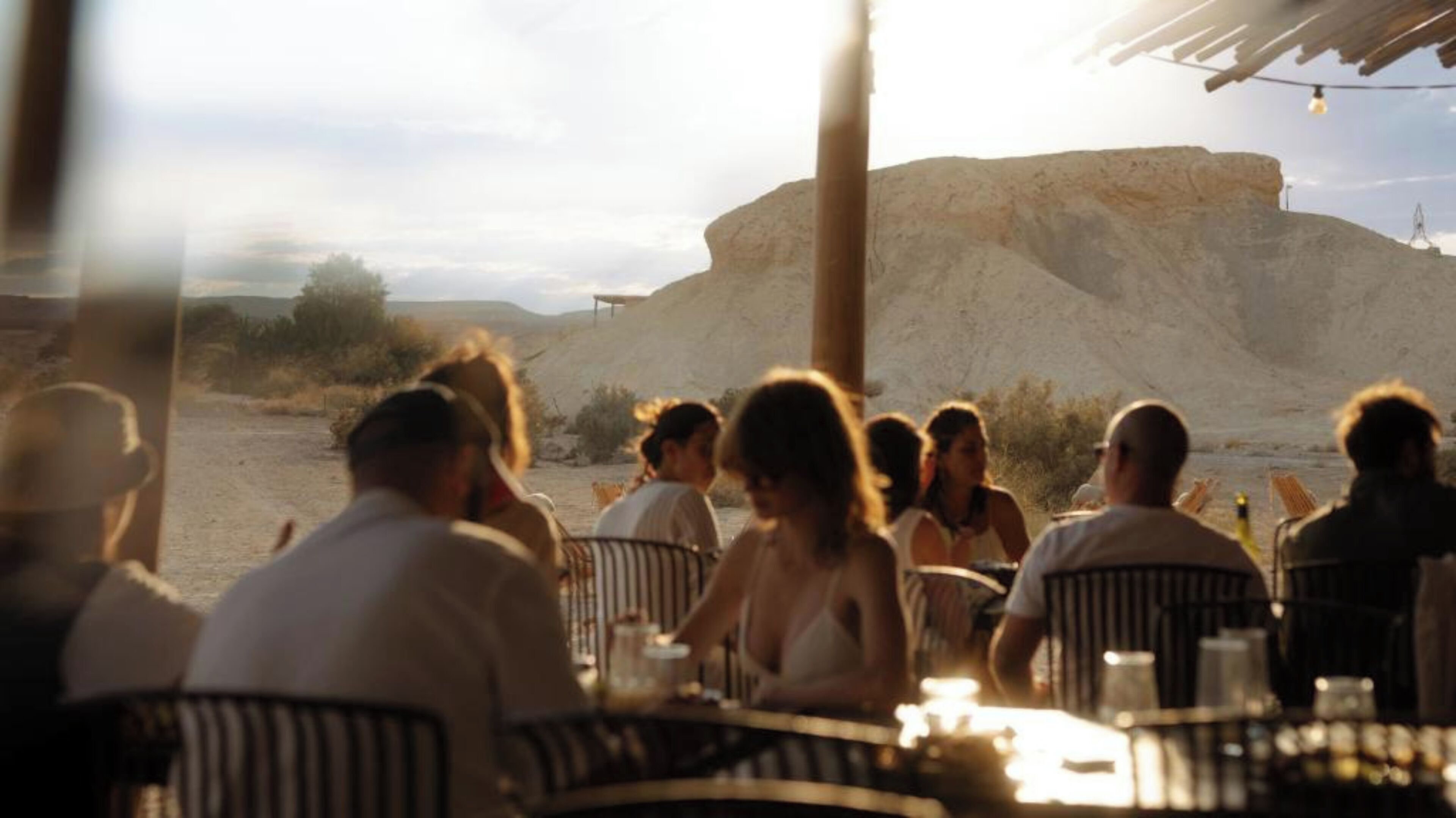 Un grupo de personas cenando al aire libre con vista a una gran formación rocosa.