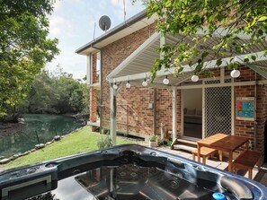 Una vasca idromassaggio con vista su un fiume, una casa in mattoni con portico coperto e un cartello di sicurezza per la piscina.