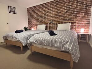 Ein Hotelzimmer mit zwei Betten, einer Ziegelwand, einem gerahmten Bild und einem Nachttisch mit einer Lampe.