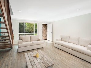 A modern living room with two sofas, a wooden coffee table, and a staircase. - Boronia House in Sawtell Creekside Townhouse (Sawtell)