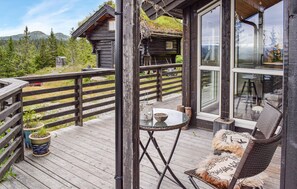 Eine Holzterrasse mit Glastür zu einem Raum, ein kleiner Tisch mit einer Schale und ein Korbstuhl.