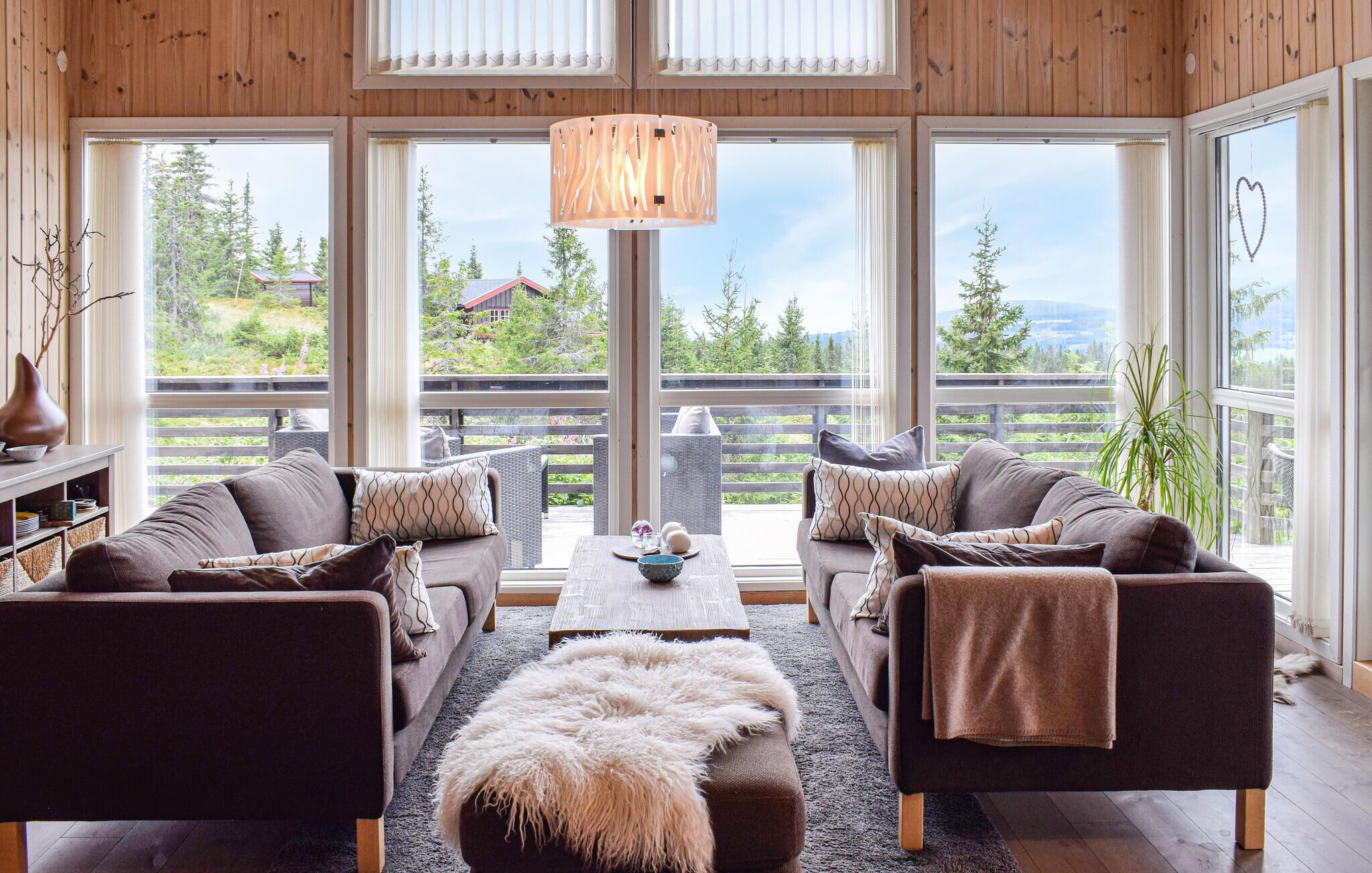 Un salon chaleureux avec un ensemble de canapés, une table basse et une grande fenêtre donnant sur des arbres et une maison.