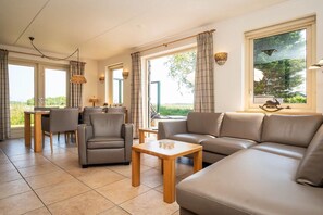 A modern living room with a sofa, chairs, a coffee table, and a dining area. - 6-Guest Texel Villa with Sauna & Spa (De Koog)