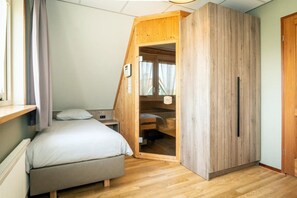 Un dormitorio con cama, un armario de madera, una ventana con cortinas y un radiador.