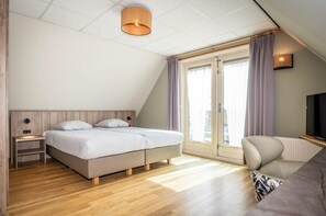 A bedroom with a bed, nightstand, TV, and a window with curtains. - 6-Guest Texel Villa with Sauna & Spa (De Koog)