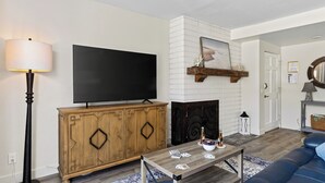 Una sala de estar con televisor de pantalla plana, mueble de madera, chimenea y un sofá azul.