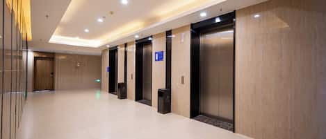A modern hotel lobby with a long corridor, elevators, and a reception area.