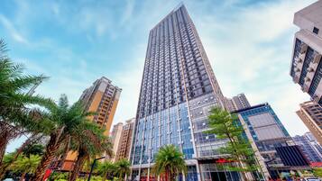 Un edificio moderno de gran altura con fachada de vidrio, rodeado de palmeras y otra vegetación.