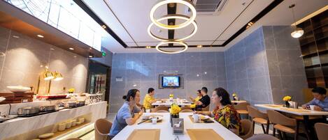 A modern dining area with round tables, a buffet, and a television screen.