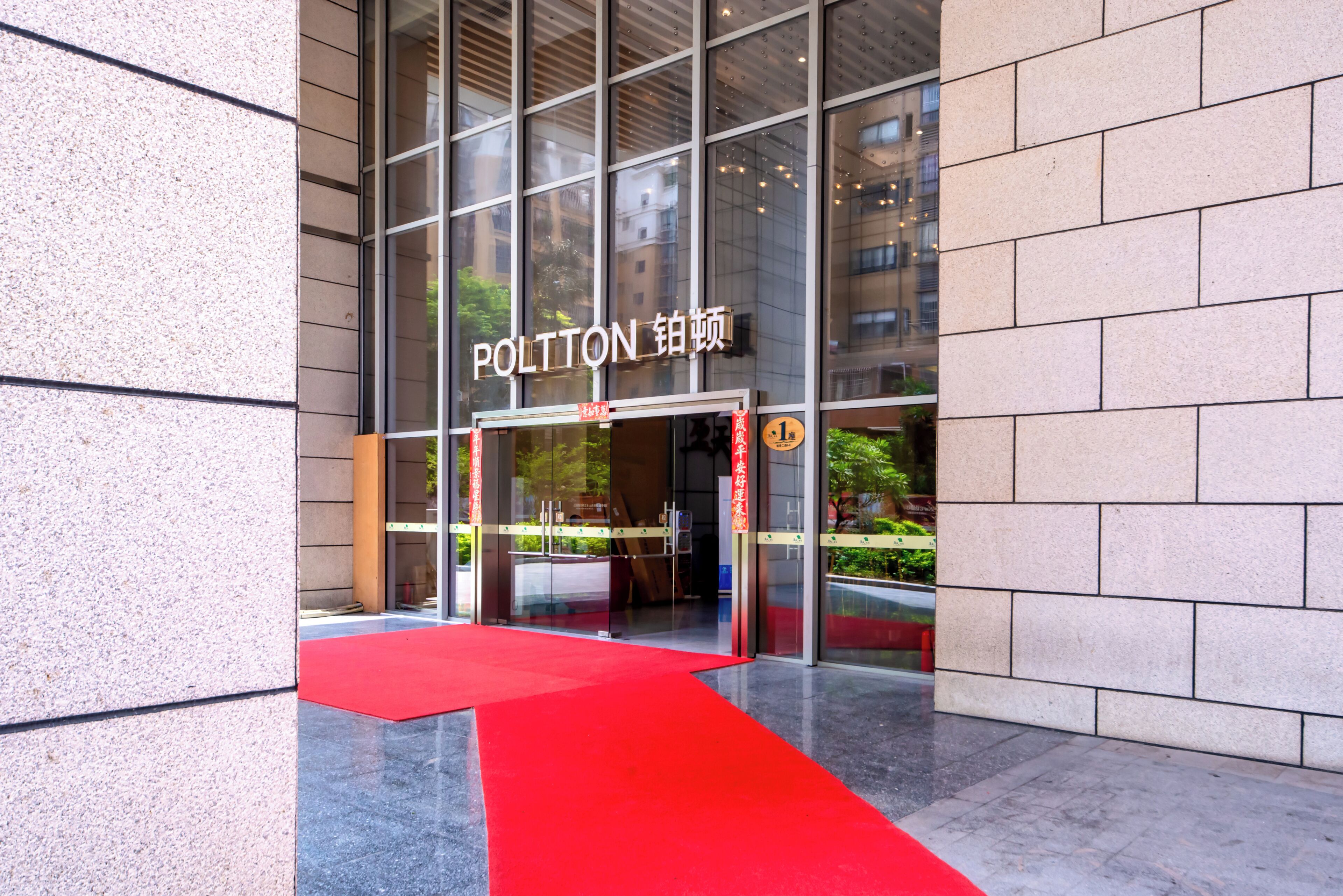 A modern building entrance with a red carpet leading to a glass door.