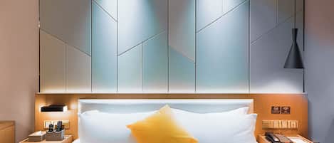 Habitación de hotel con cama, mesita de noche con teléfono y lámpara, pared con lámpara y señal que indica disponibilidad de WiFi.