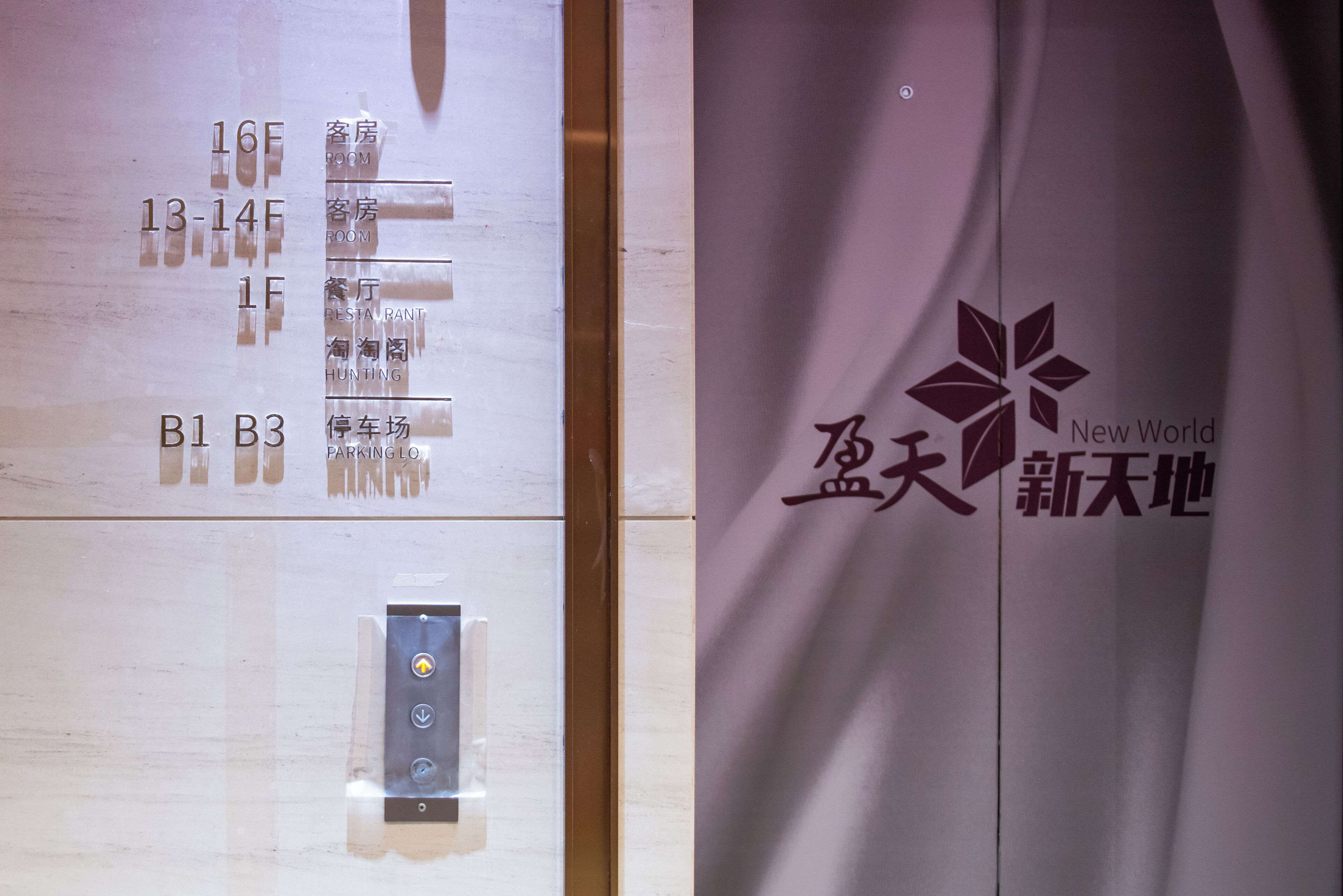 A hotel elevator with floor labels and a New World logo.