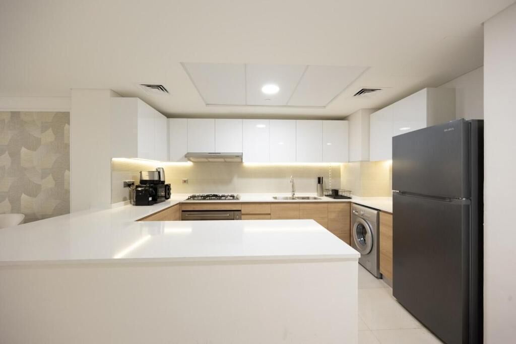 A modern kitchen with white cabinetry, a central island, a washing machine, and a black refrigerator.