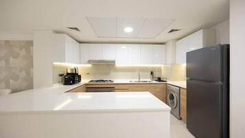 A modern kitchen with white cabinetry, a central island, a washing machine, and a black refrigerator.
