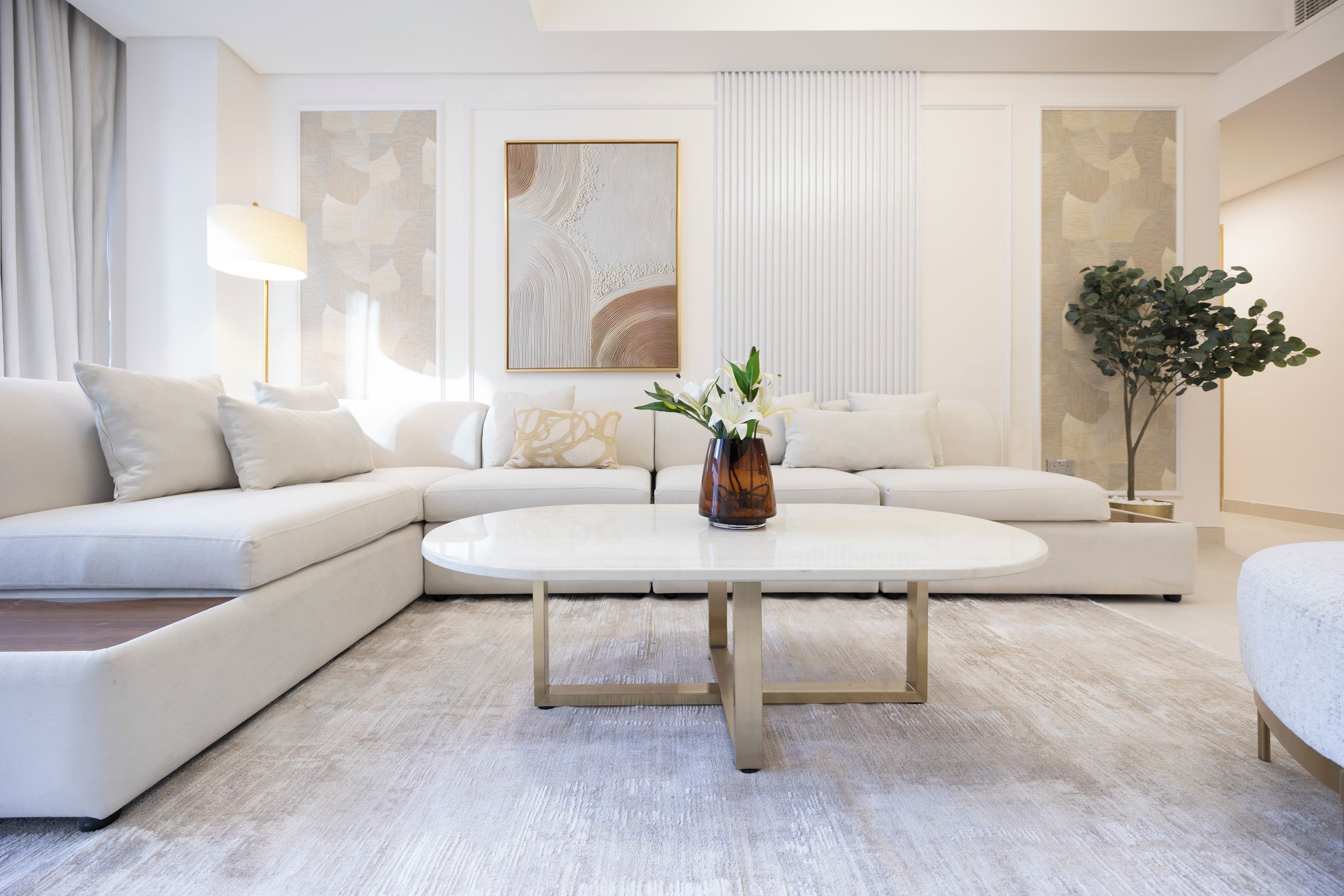 A modern living room with a white sofa, a coffee table, and a vase with flowers.