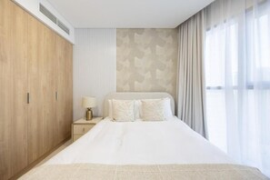 A hotel room with a large bed, a wardrobe, a nightstand with a lamp, and a window with curtains.
