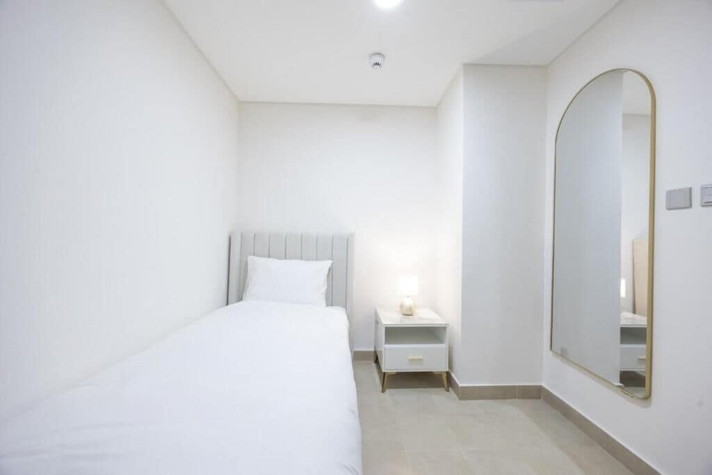 Une chambre à coucher comprenant un lit, une table de chevet, une commode et un grand miroir au mur.