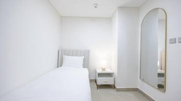 A bedroom with a bed, bedside table, nightstand, and a large mirror on the wall.