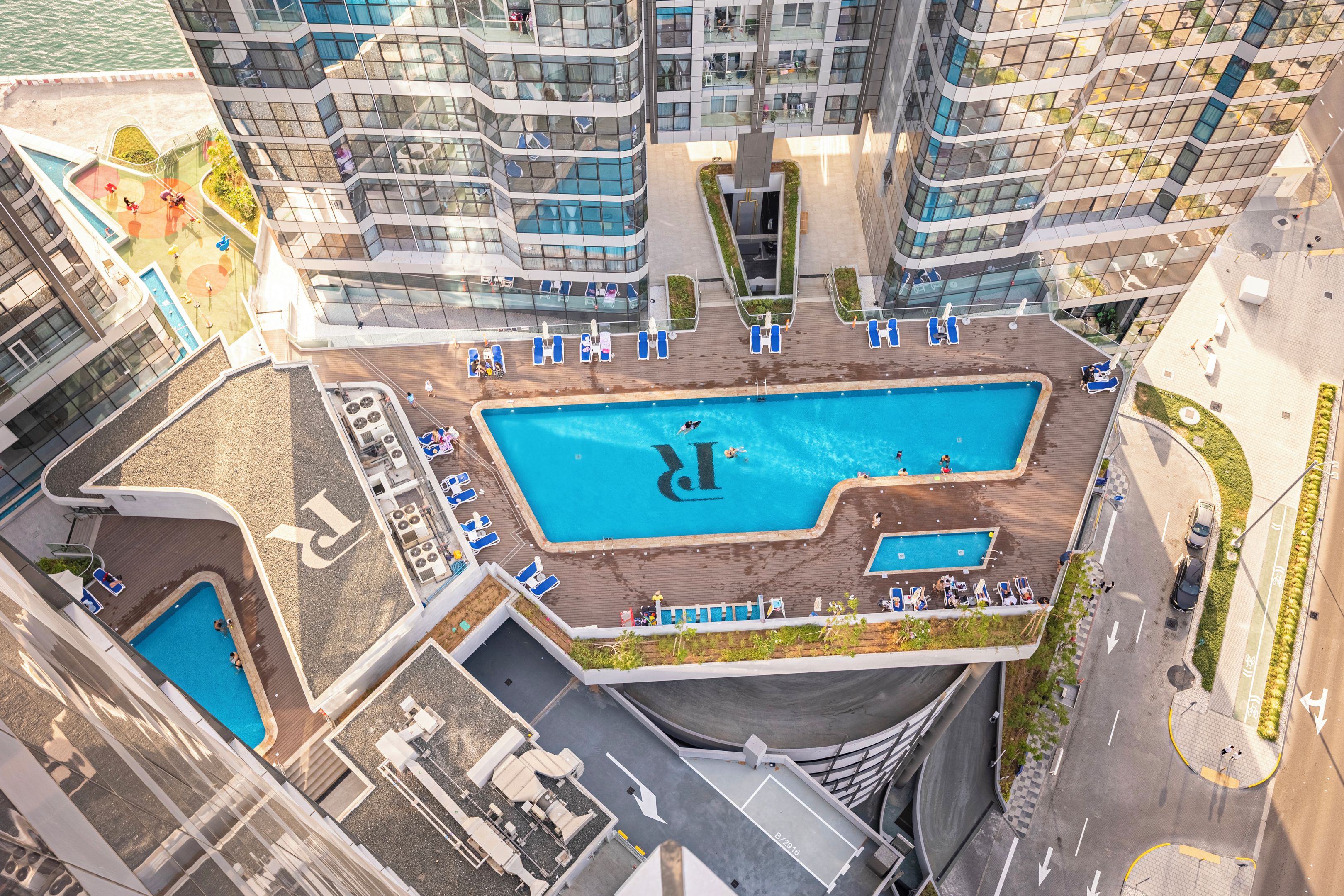 A high-rise building with a rooftop pool surrounded by lounge chairs and a smaller pool.