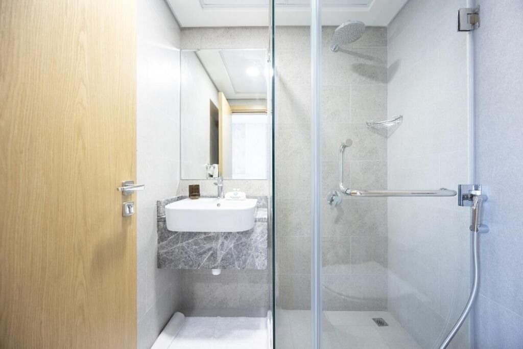 A modern bathroom with a glass shower enclosure, a marble sink, and a wooden door.