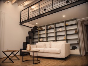 A modern living room with a sofa, a coffee table, a bookshelf, and a staircase. - The Hidden Passage by LOC Hospitality (Kerkyra)