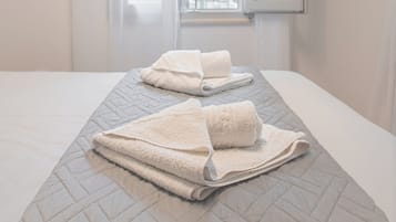 Habitación de hotel con cama, dos toallas, una ventana con cortinas y vistas a edificios.