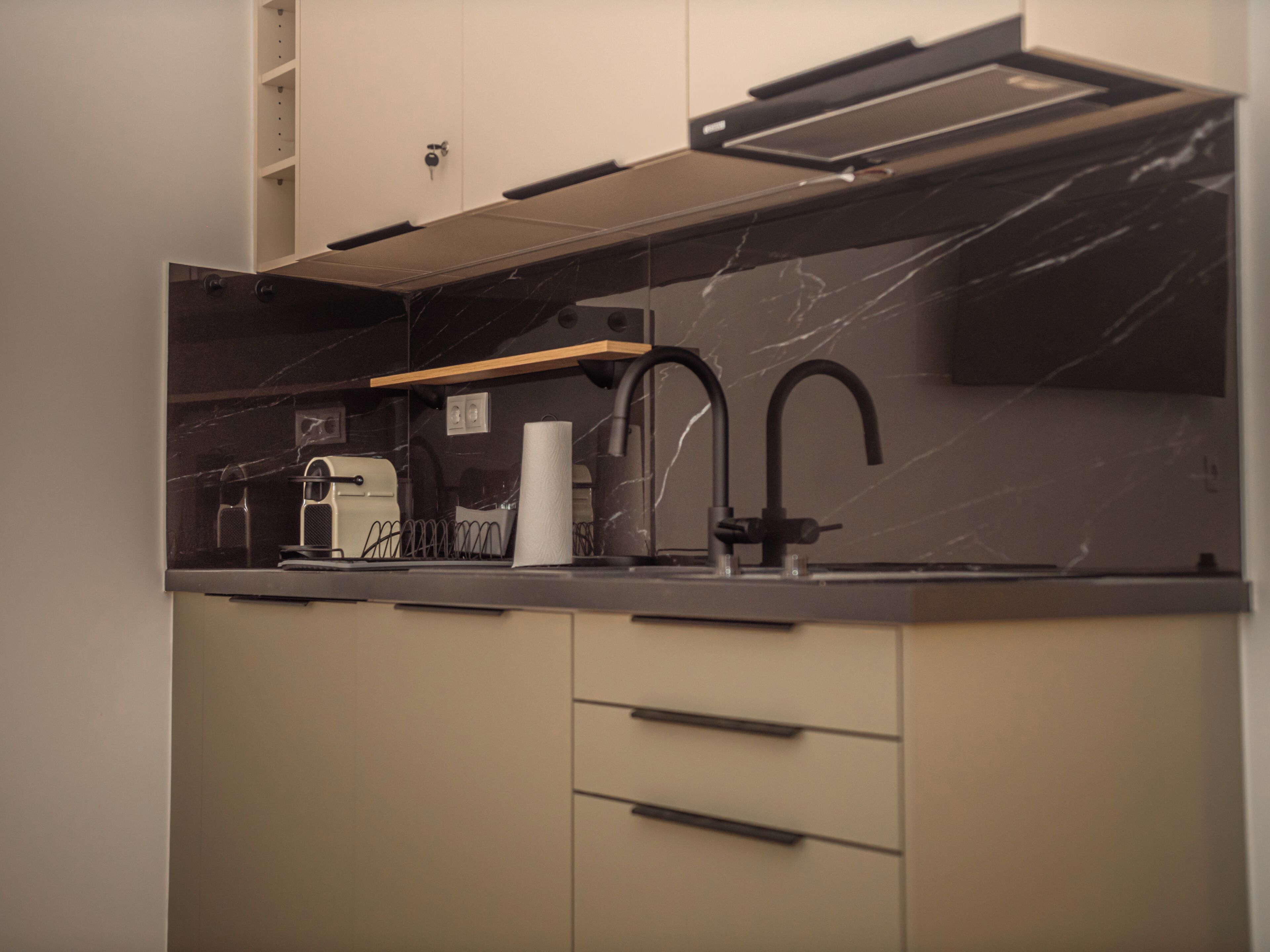 A modern kitchen with a black countertop, a built-in oven, a coffee machine, and a paper towel dispenser.