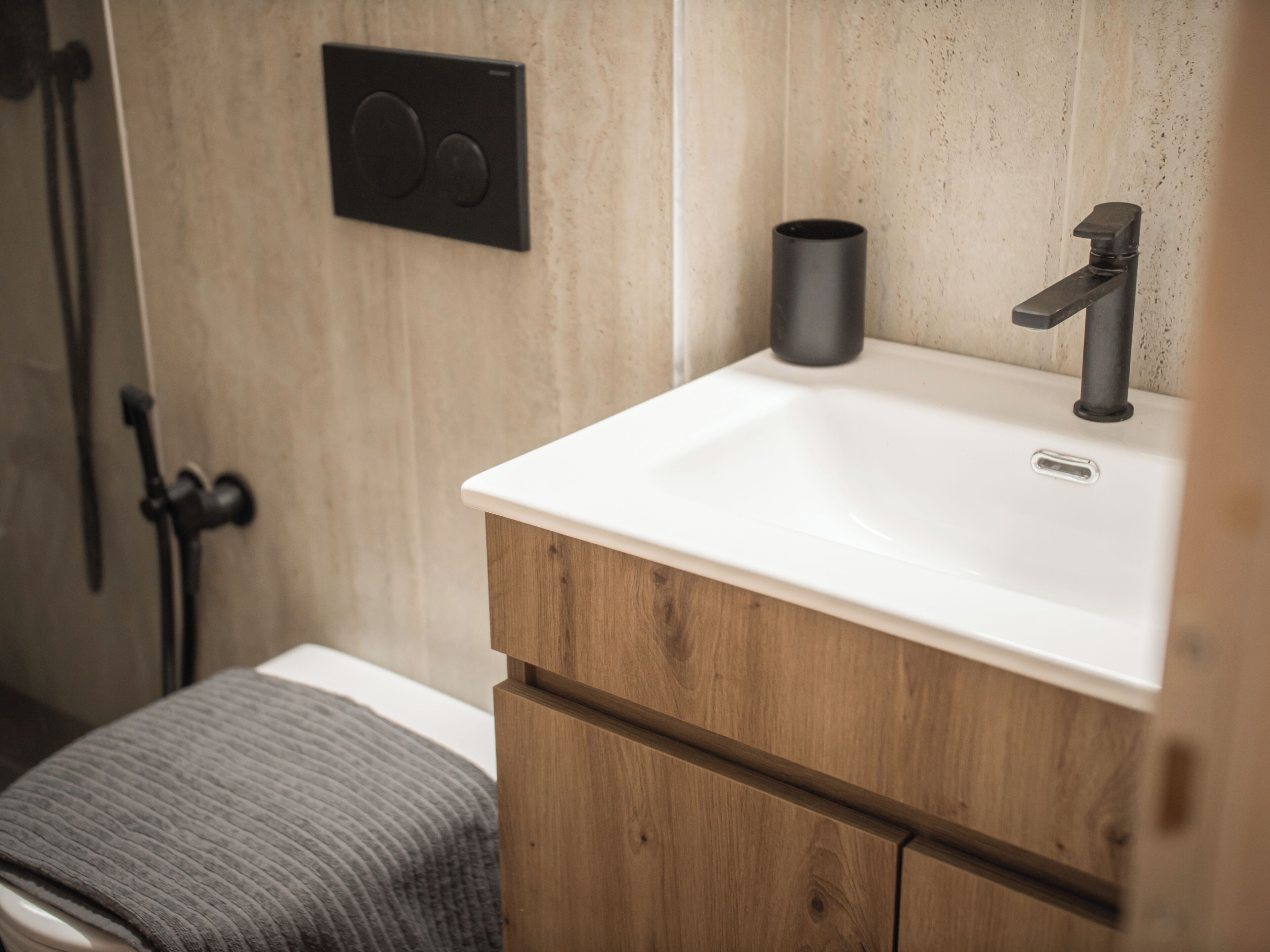 A bathroom with a wooden vanity, a white sink, a black faucet, and a black cup on the sink.